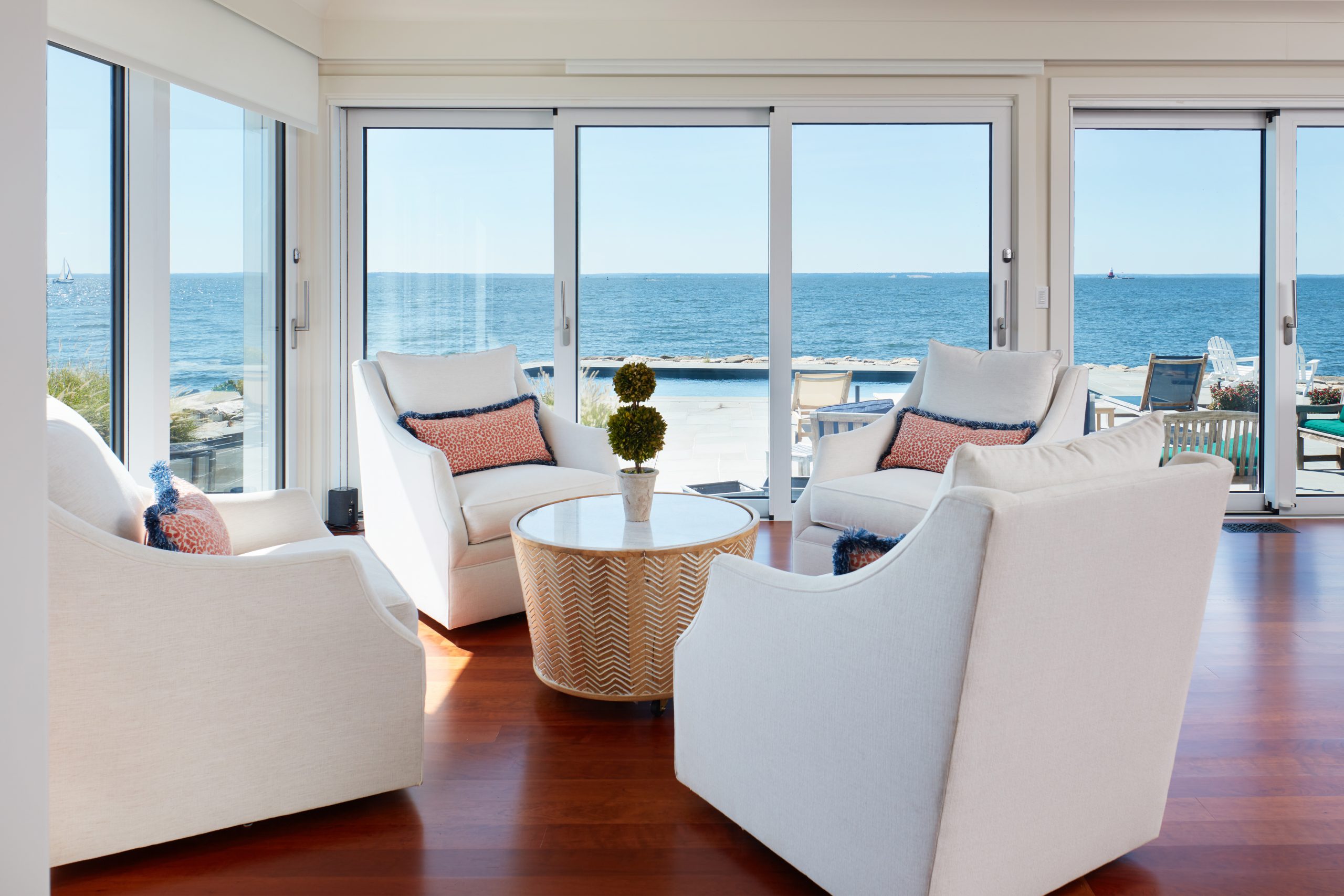 Belle Island lounge area corner with four sofa chairs and a coffee table in the middle, surrounded by two walls of sliding glass doors that look out to to the pool and long island sound